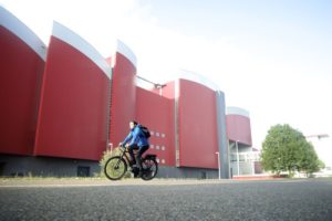 man op e-bike voor een rood gebouw